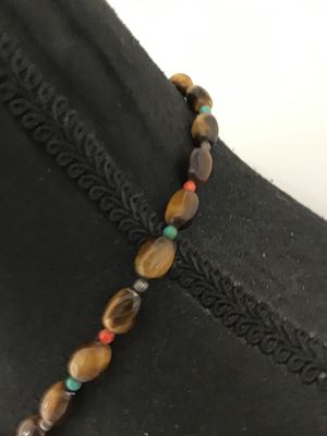 Sale Photo Thumbnail #19: A beaded gemstone necklace featuring smooth, polished tiger's eye oval beads accented with small turquoise and red/coral-tone spacer beads and silver-tone fluted metal spacers. Finished with a decorative silver-tone toggle closure clasp. In good pre-owned