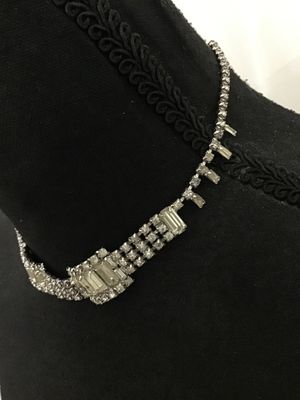 Sale Photo Thumbnail #288: Vintage silver-tone rhinestone choker necklace featuring a central panel of baguette and round-cut clear stones, flanked by multi-strand detail and dangling baguette accents. Features an adjustable hook clasp with extension tail. Shows minor light age-app