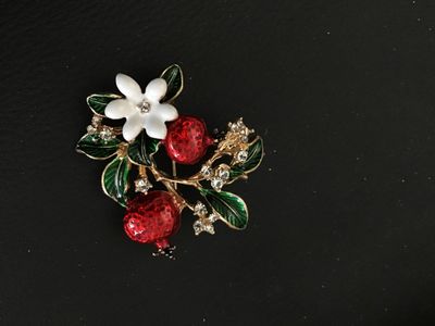 Sale Photo Thumbnail #75: Gold-tone floral brooch featuring red enamel pomegranates, green enamel leaves, a white flower, and clear rhinestone accents. Includes a standard pin back with locking clasp. In good pre-owned condition with no missing stones observed.