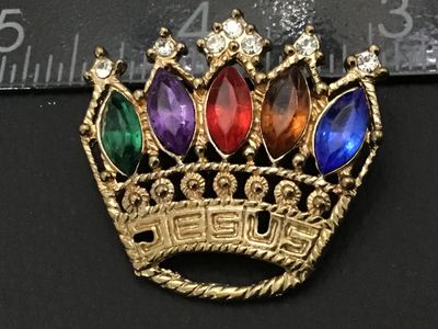 Sale Photo Thumbnail #86: Gold-tone metal brooch featuring a crown design with 'JESUS' spelled along the band. Set with multi-colored navette rhinestones in green, purple, red, topaz, and blue, topped with clear accent rhinestones. Measures approximately 1.5 inches wide. Standard 