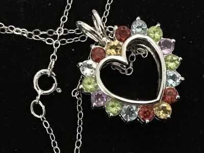 Sale Photo Thumbnail #139: A sterling silver heart-shaped pendant necklace featuring a reversible design. One side is adorned with multi-color round faceted gemstones including amethyst, peridot, citrine, garnet, and blue topaz, while the reverse side features a halo of uniform lig