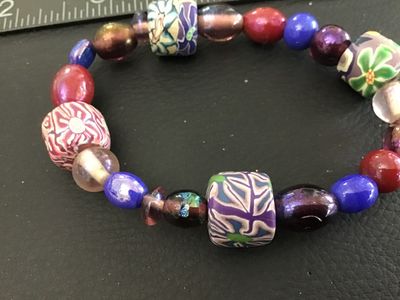 Sale Photo Thumbnail #48: Multicolor beaded stretch bracelet featuring patterned polymer clay millefiori-style focal beads alongside vibrant glass and iridescent beads in shades of purple, blue, red, and green. Measures approximately 2.5 inches in diameter resting relaxed. Good co