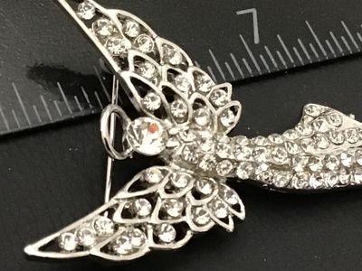 Sale Photo Thumbnail #227: Silver-tone metal brooch designed in the shape of a winged guardian angel with a halo, densely set with clear rhinestones throughout the body and openwork wings. Features a standard pin back with rollover safety clasp. Measures approximately 2.25 inches i