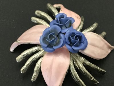Sale Photo Thumbnail #179: Vintage silver-tone metal floral brooch featuring three blue dimensional rose buds at the center, surrounded by pale pink enamel leaves and textured silver-tone tendrils/stems. Secured with a standard rollover safety clasp on the back. Shows minor enamel 