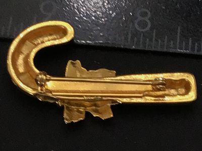 Sale Photo Thumbnail #216: A festive gold-tone holiday brooch featuring a candy cane motif with red and white enamel detailing, accented by green and red enamel holly leaves and berries at the center. Standard pin stem with safety clasp on back. Measures approximately 2 inches long