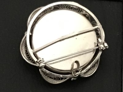 Sale Photo Thumbnail #158: A vintage silver-tone filigree brooch featuring a center domed cabochon with an embedded orange botanical/flower design. The back features a standard pin bar mechanism along with a small bail, allowing it to be worn as either a brooch or a pendant. Measur
