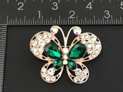 Sale Photo Thumbnail #46: A gold-tone butterfly pin/brooch featuring teardrop emerald green faceted glass stones, clear rhinestones, and iridescent aurora borealis rhinestones along the antennae and center body. Features openwork filigree details on the wings and a standard pin ba