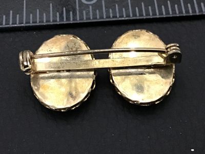 Sale Photo Thumbnail #200: A vintage double-oval brooch featuring hand-painted or transfer porcelain cabochons set in gold-tone metal. Each oval displays a colorful bird perched on a floral branch. Measures approximately 1.25 inches across. The pin back and C-clasp are in functiona