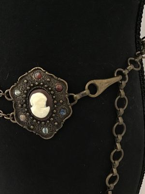Sale Photo Thumbnail #259: A vintage brass-tone chain belt featuring a central ornate pendant set with a portrait cameo insert and surrounding multi-color cabochon accents. The chain strand includes additional bezel-set multi-colored faux stones and a hook clasp closure with decora