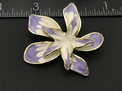 Sale Photo Thumbnail #96: A floral brooch featuring layered petals in light purple and white enamel with gold-tone edging. The back shows a textured gold-tone finish with a standard pin stem and rollover safety clasp. Measures approximately 2.25 inches across. Overall good pre-own