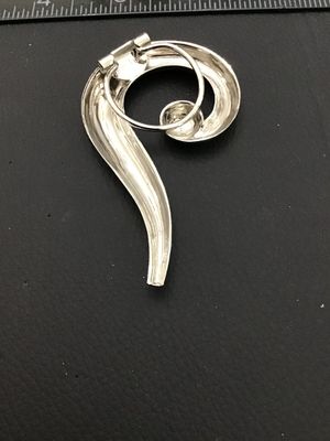 Sale Photo Thumbnail #252: A vintage silver-tone scarf clip brooch featuring an abstract swirl design with a central accent sphere. Marked 'VERA-LU' on the back mechanism. Measures approximately 3 inches in length and 1.5 inches in width. In good condition with minimal surface wear