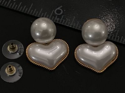 Sale Photo Thumbnail #230: Pair of gold-tone post earrings featuring round white faux pearl studs with dangling, beaded-edge heart charms filled with a matching pearlescent finish. Includes plastic clutch backs. Condition is very good with light surface wear.