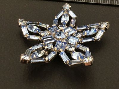 Sale Photo Thumbnail #104: A vintage star or snowflake-shaped costume jewelry brooch pin featuring light blue and clear faceted rhinestones. The piece is set with baguette, marquise, and round-cut stones in a silver-tone metal setting. Includes a standard pin stem and rollover clas