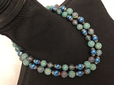 Sale Photo Thumbnail #61: A mid-century vintage double strand necklace featuring a combination of bright blue satin glass pearls, textured light blue sugar beads, and clear glass beads with red and gold foil speckles. Includes filigree metal bead caps and a decorative box clasp fe