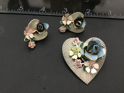 Sale Photo Thumbnail #267: A vintage Coro costume jewelry set featuring a heart-shaped brooch pin and matching clip-on earrings. Design features silver-tone ribbed metal hearts adorned with colorful enamel flowers (blue, pink, yellow) and clear rhinestone accents. The clip-on earri