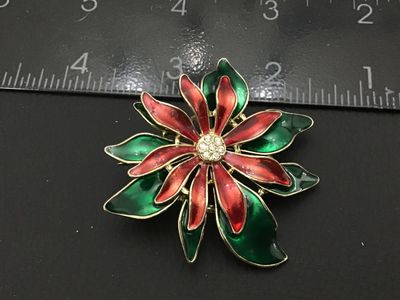 Sale Photo Thumbnail #154: A festive vintage gold-tone brooch shaped like a poinsettia flower featuring red and green enamel layered petals. The center is detailed with a cluster of small sparkling clear rhinestones. Features a standard pin back clasp mechanism. Measures approximat
