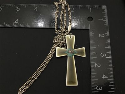 Sale Photo Thumbnail #147: Vintage enamel cross pendant necklace featuring a flared cross design with hand-painted style enamel detail in turquoise, pink, and gold tones over an olive-tan background. The chain clasp is marked CELEBRITY. The pendant measures approximately 3 inches i