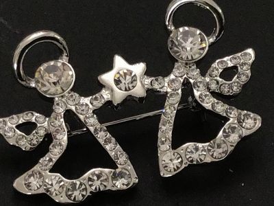 Sale Photo Thumbnail #89: Silver-tone costume jewelry pin/brooch featuring two winged angels holding a central star, fully encrusted with clear, faceted rhinestones. Fitted with a rollover safety clasp on the back. Measures approximately 2 inches wide. Excellent condition with all