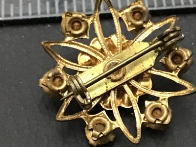 Sale Photo Thumbnail #286: Vintage gold-tone brooch featuring a central bright red rhinestone framed by faux pearls, surrounded by dark red/garnet-colored rhinestone accents in a starburst or flower motif. Shows slight vintage wear and patina to the gold-tone metal on the back. Fea