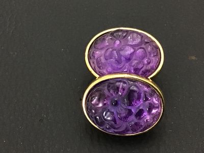 Sale Photo Thumbnail #164: Pair of vintage gold-tone oval clip-on earrings featuring carved purple glass inserts with floral patterns. Each earring measures approximately 0.75 inches long. Backs feature a textured sunburst finish and clip mechanisms. Light vintage wear to metal fin