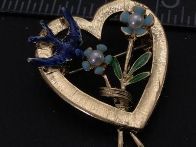 Sale Photo Thumbnail #110: Vintage gold-tone openwork heart brooch featuring a blue enamel bird, enamel flowers with faux pearl centers, and green leaf accents. Features textured gold-tone finish on the front and a standard pin back with rollover clasp. Measures approximately 1.25 
