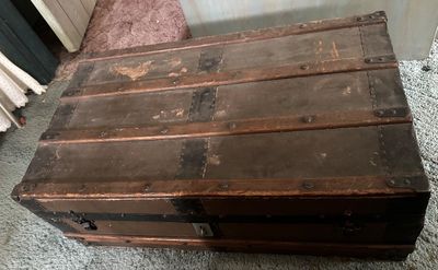 Sale Photo Thumbnail #169: Antique flat-top steamer trunk featuring wooden slats, metal hardware, and a weathered finish.