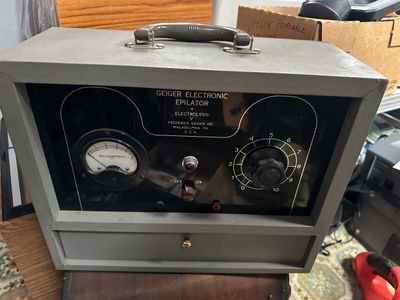 Sale Photo Thumbnail #62: Vintage Geiger Electronic Epilator unit by Frederick Geiger Inc. housed in a gray metal carrying case with a milliamperes meter gauge.