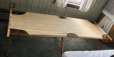 Sale Photo Thumbnail #173: Vintage military-style folding camp cot with a sturdy wooden frame and heavy tan canvas top.