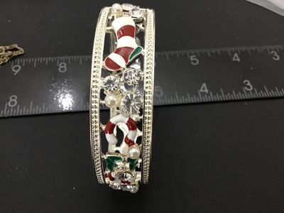 Sale Photo Thumbnail #185: Silver-tone hinged cuff bangle bracelet featuring holiday-themed enamel motifs including Christmas stockings and candy canes, accented with clear rhinestones and imitation pearls. Measures approximately 2.5 inches in diameter with a spring hinge closure. 