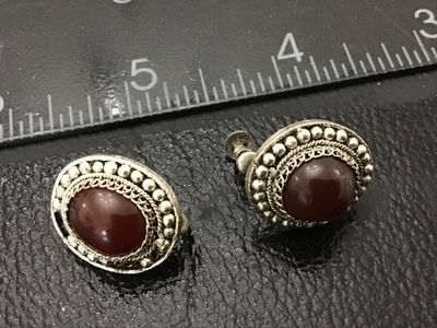 Sale Photo Thumbnail #165: Pair of vintage silver-tone screw-back earrings featuring intricate filigree work, beaded borders, and polished dark red/carnelian-style cabochon stones. Oval face measures approximately 0.75 inches long. Light patina consistent with age; overall good vin