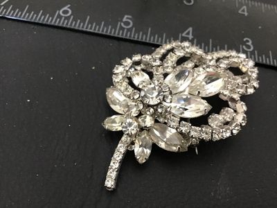 Sale Photo Thumbnail #89: Vintage silver-tone brooch featuring clear marquise and round cut rhinestones arranged in a floral floral spray and ribbon loop design. Measures approximately 2.5 inches in length. Features a rollover safety clasp on the back. Unmarked. In good vintage co