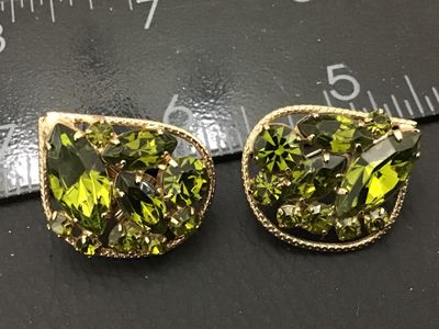 Sale Photo Thumbnail #27: Pair of vintage gold-tone clip-on earrings featuring marquise and round-cut olive green rhinestones set within a textured border. Each earring measures approximately 1 inch across. In good condition with functional clip backs and intact stones.