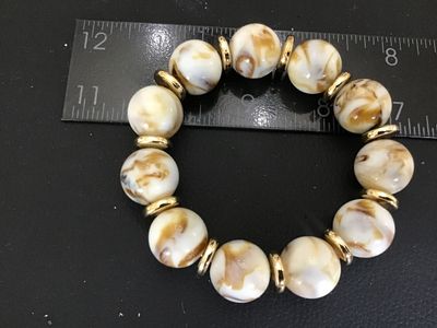 Sale Photo Thumbnail #53: A stretch beaded bracelet featuring marbled cream and light brown swirled round beads separated by gold-tone disc spacers. The bracelet measures approximately 2.5 to 3 inches in outer diameter.