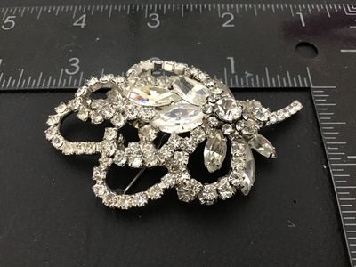 Sale Photo Thumbnail #86: Vintage silver-tone brooch featuring clear marquise and round cut rhinestones arranged in a floral floral spray and ribbon loop design. Measures approximately 2.5 inches in length. Features a rollover safety clasp on the back. Unmarked. In good vintage co