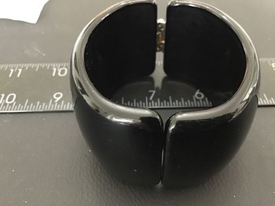 Sale Photo Thumbnail #37: A wide, glossy black acrylic or plastic hinged cuff bracelet. Features a spring hinge design for easy wear. Measures approximately 2 inches wide. Good pre-owned condition with light surface wear visible upon close inspection.