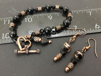 Sale Photo Thumbnail #54: Matching costume jewelry set including a beaded bracelet and pair of dangle hook earrings. Features black round and faceted glass beads, copper-tone filigree metal spacer beads, and a heart-shaped toggle clasp on the bracelet. Bracelet measures approximat