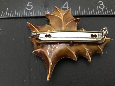 Sale Photo Thumbnail #103: Vintage Christmas brooch featuring molded tan/brown holly leaves with shiny red bead berries. Constructed from molded plastic/celluloid material with a silver-tone metal pin back mechanism. Measures approximately 2 inches wide by 1.75 inches tall. Shows m