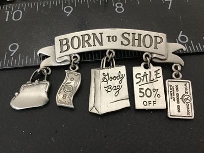 Sale Photo Thumbnail #66: A vintage silver-tone pewter novelty brooch by Jonette Jewelry (JJ) featuring a 'BORN TO SHOP' banner with five dangling shopping-themed charms: a coin purse, five-dollar bill, goody bag, 'Sale 50% Off' sign, and a credit card. Marked '©JJ' on the revers