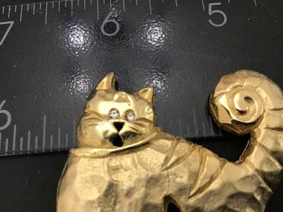 Sale Photo Thumbnail #83: Vintage gold-tone cat brooch by Ultra Craft featuring a hammered texture, curly tail, small rhinestone eyes, and a mouse accent near the bottom edge. Marked ULTRA CRAFT on the back. Measures approximately 2 inches wide by 2 inches tall. In good vintage co