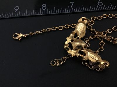 Sale Photo Thumbnail #197: Vintage Avon gold-tone necklace featuring a ornate scrollwork centerpiece with pink porcelain roses, green leaf accents, faux pearl details, and a central pink oval crystal stone. Signed Avon on the back of the pendant and on the hangtag. Fitted with a lo