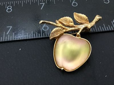Sale Photo Thumbnail #17: A vintage Sarah Coventry gold-tone brooch shaped like an apple on a leafy branch. Features a satin iridescent pearlescent cabochon apple insert. Signed SARAH COV on the back. Pin mechanism in good working condition. Measures approximately 1.75 inches long