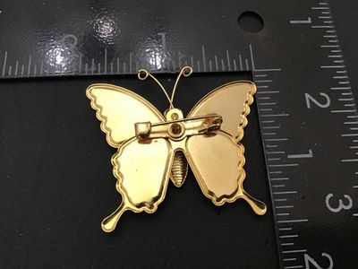 Sale Photo Thumbnail #20: Gold-tone metal butterfly brooch featuring colorful red, orange, and gold glitter inlay or enamel fill on the wings. Measures approximately 2 inches wide by 2 inches tall. Features a standard rollover safety pin closure on the back. Good pre-owned conditi