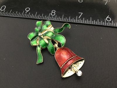 Sale Photo Thumbnail #214: A festive gold-tone Christmas brooch featuring a green enamel bow and a dangling red enamel bell decorated with clear rhinestone accents. Measures approximately 2 inches long. Good vintage condition with light surface wear.