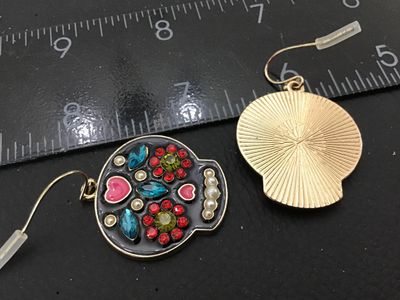 Sale Photo Thumbnail #65: Pair of gold-tone sugar skull (Calavera) dangle earrings featuring black enamel with colorful rhinestone and faux pearl accents. Equipped with french wire hooks and plastic safety backs. Skull pendants measure approximately 1 inch in width. Good condition