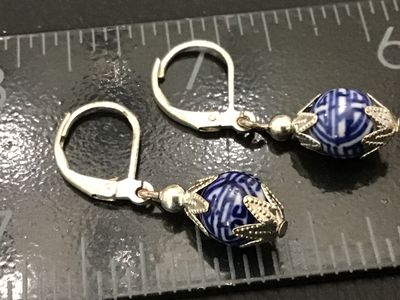 Sale Photo Thumbnail #172: Pair of dangle earrings featuring round blue and white porcelain beads with detailed geometric/Asian inspired patterns, set in silver-tone filigree metal end caps. Designed with leverback closures for secure wearing. Each earring measures approximately 1.
