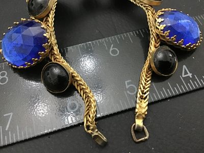 Sale Photo Thumbnail #137: Vintage gold-tone woven snake/fox tail chain bracelet featuring large faceted cobalt blue glass stones in crown prongs alternating with smooth black cabochon accent stones. Total length is approximately 7.5 inches as shown against the ruler. Metal shows l