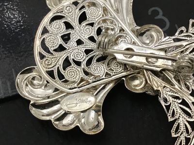 Sale Photo Thumbnail #160: A detailed silver tone vintage brooch designed in the shape of an angel with intricate openwork filigree and a central clear faceted rhinestone. Marked 'Janvis' on the reverse oval cartouche. Features a standard pin back closure. Measures approximately 2.