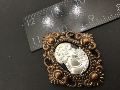 Sale Photo Thumbnail #39: Vintage brooch pin featuring a silver-tone/pewter-style woman's portrait cameo set in an ornate bronze-tone Faux metal frame with scrolling openwork design. The reverse shows a glued-on bar pin back mechanism. Measures approximately 2 inches tall by 1.5 i