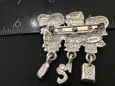 Sale Photo Thumbnail #115: Silver-tone metal brooch featuring three children spelling out "I [Heart] My Teacher" with hanging charms depicting a math book, ABCs, and a pencil. Hand-painted enamel details in various colors. Marked "© AJMC" on the back. Standard pin stem with lockin