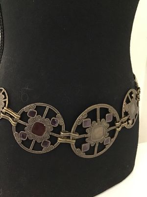 Sale Photo Thumbnail #158: Vintage brass-tone chain link belt featuring ornate openwork circular medallions inset with purple and brown glass or acrylic cabochons. Includes an adjustable hook and tail extension chain. Shows light finish wear and patina consistent with age.